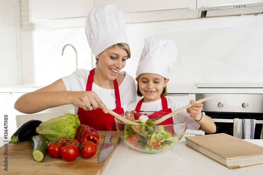 mother and little daughter cooking together with hat apron preparing salad at home kitchen mother and little daughter cooking together with hat apron preparing salad at home kitchen