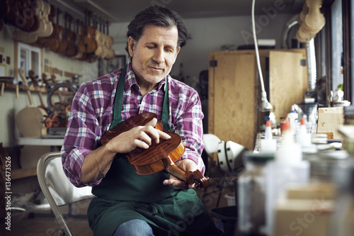 Worker touching violin while working in workshop photo