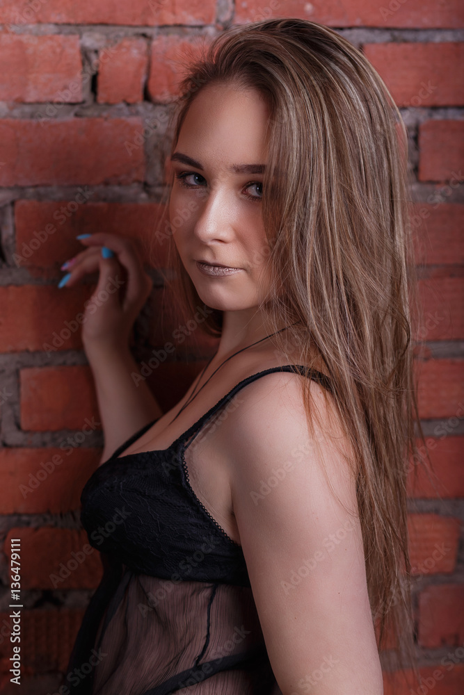 Fototapeta premium portrait of beautiful girl blonde with delicate make-up near brick wall looking at the camera in black lingerie