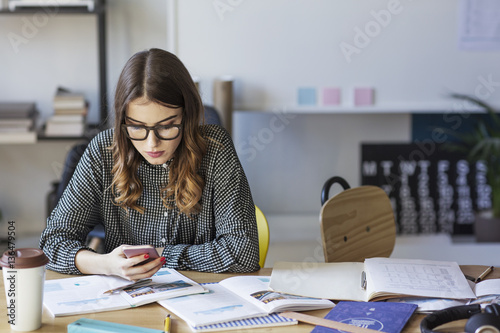 Woman using smart phone while sitting at table in college photo