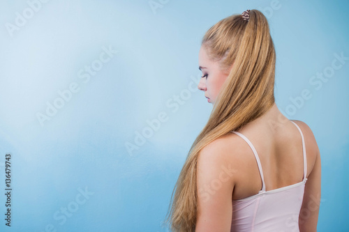 beautiful blonde girl with gum collected in long hair is profile on a blue background with her head looking down from copyspace