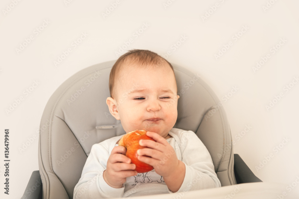 Cute baby girl sitting on high children chair and eating fruit apple Cute baby girl sitting on high children chair and eating fruit apple