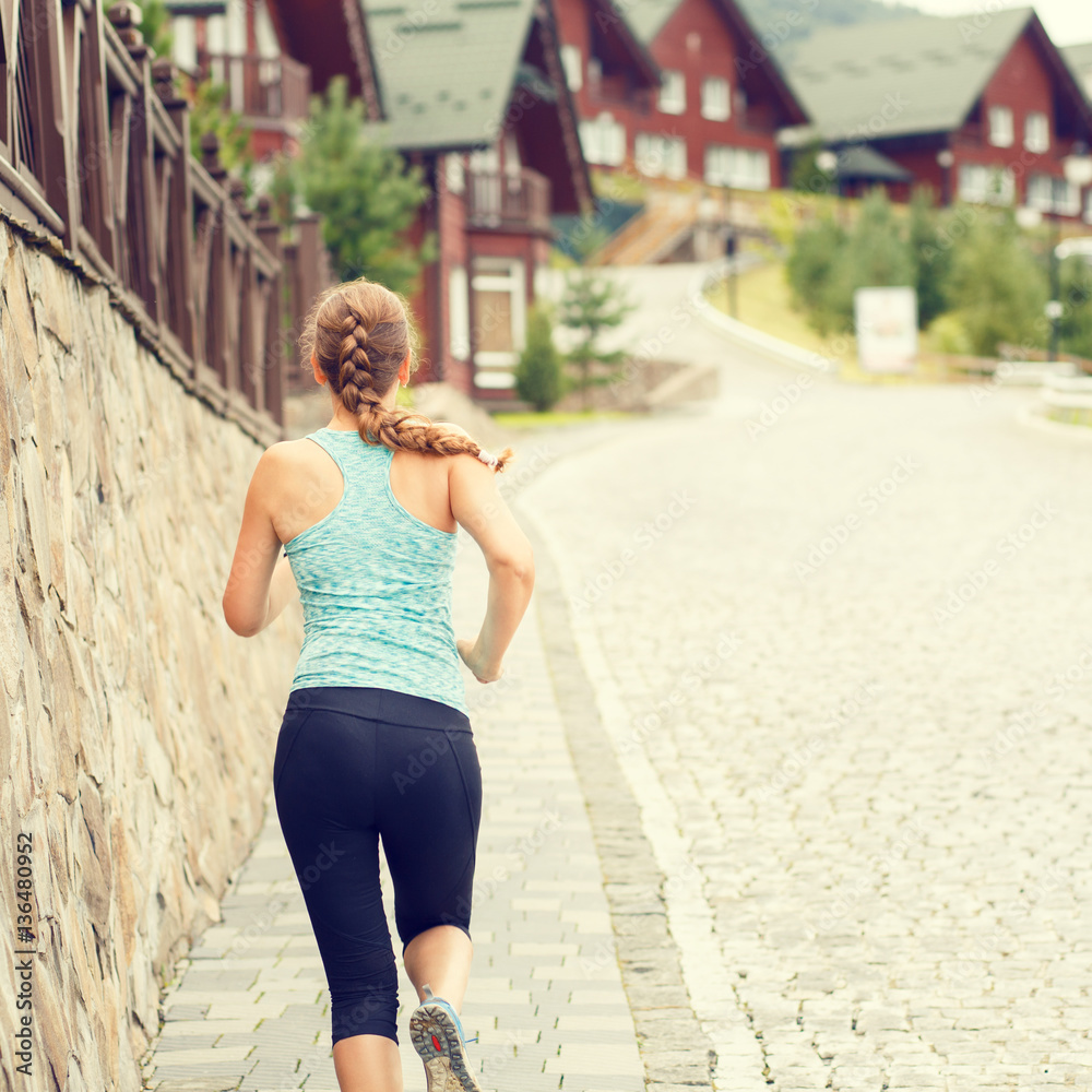 Athletic girl running on cobbled street in mountains europe town. Warm color toned image of fitness jogging woman