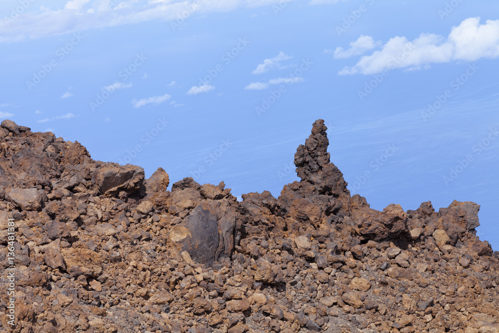 Brown volcanic rocks piled on a mountain edge, against cloudy blue sky