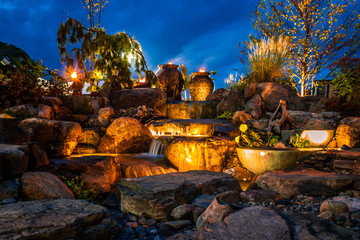 Leinwandbilder Schwarz Waterfall fountain landscape at night with gold color lights and tiki  © rabbitti