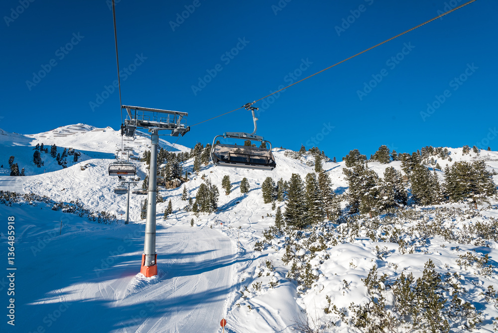 Obraz premium Ski lift with seats going over the mountain and ski tracks