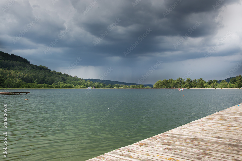 Wooden bridge on the lake in a mountain valley, storm clouds