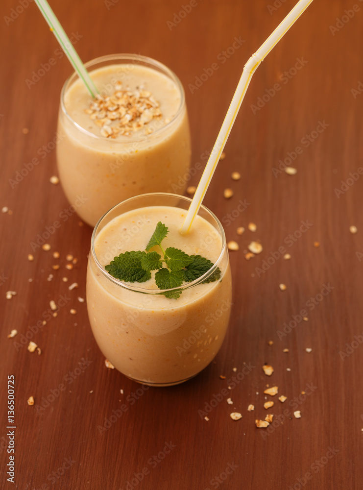 On a brown background with two glasses of drinking cream, cereal and pieces of fruit. Banana smoothie - orange. Healthy eating.