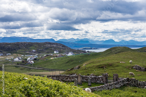Fototapeta Naklejka Na Ścianę i Meble -  Assynt Peninsula, Scotland - June 7, 2012: The hamlet of Lochinver sits on the shore of Loch Inver an arm of the Atlantic Ocean. Blue-gray cloudscape and green pasture upfront. Horizon of mountains.