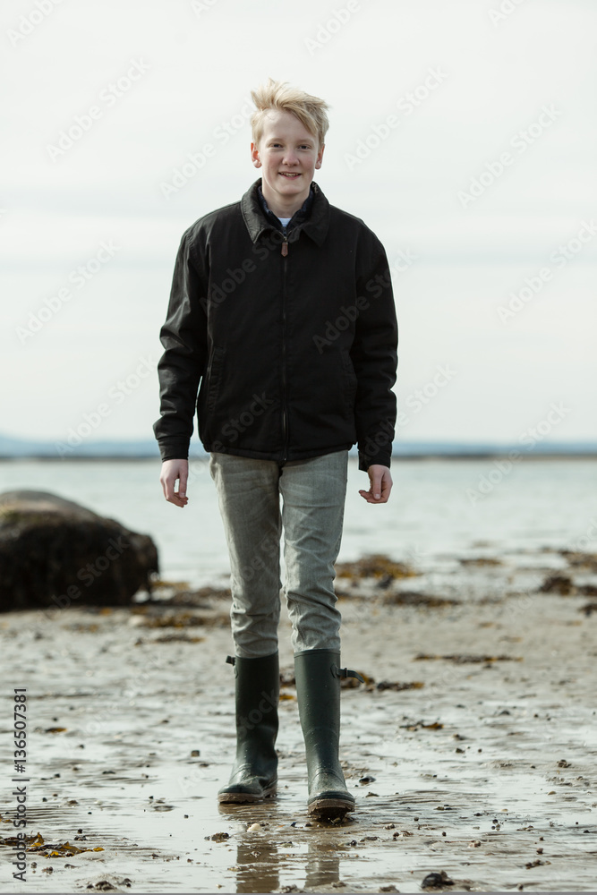 Young man in boots and jacket walking on beach Young man in boots and jacket walking on beach