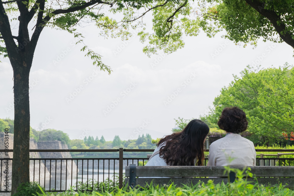 Back of two women sitting and talking on wood bench