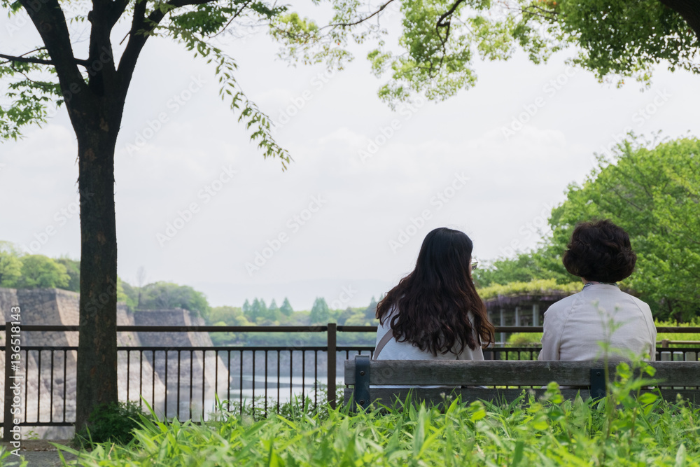 Back of two women sitting and talking on wood bench