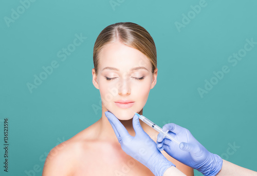 Doctor injecting botox in a beautiful face of a young woman. Pla