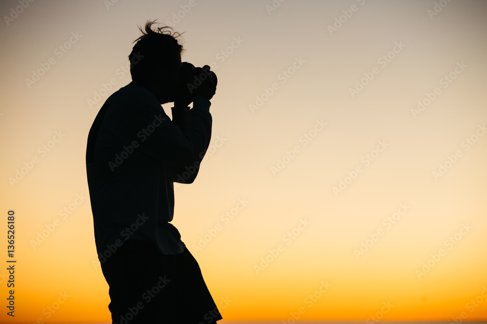 Silhouette of a handsome photographer student taking photo of sunset at ocean shore for a contest of project.