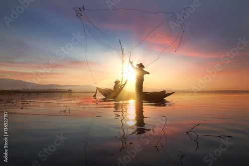 Silhouette of fishermen using nets to catch fish at the Bangpra lake with beautiful scenery of nature during sunrise time. Bang Pra Reservoir at Chonburi province in Thailand photo