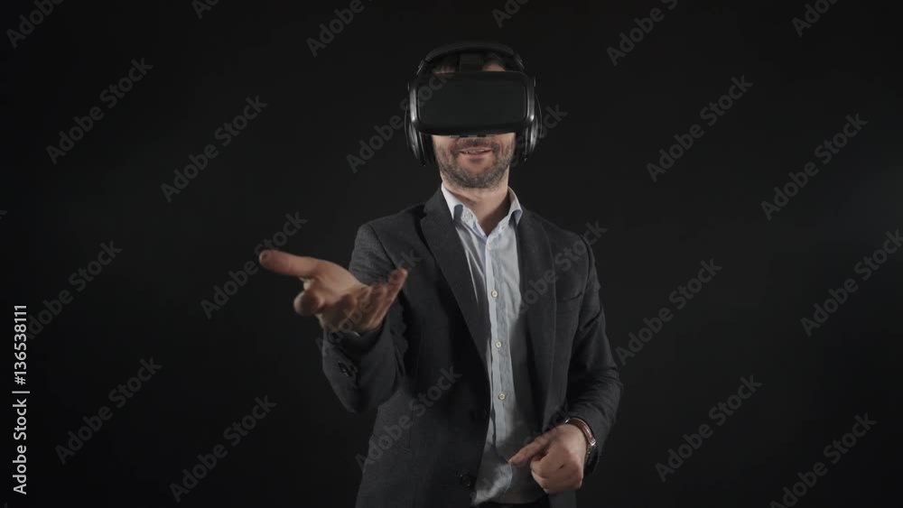 Man in suit uses virtual reality goggles. Black background. Man uses virtual interface. High-tech devices. The movement of the hands on a black background. Virtual reality helmet with headphones. 4K
Man in suit uses virtual reality goggles. Black background. Man uses virtual interface. High-tech devices. The movement of the hands on a black background. Virtual reality helmet with headphones. 4K