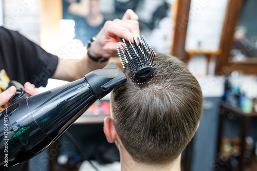 Master cuts hair of men in the barbershop, hairdresser makes hairstyle for a young man