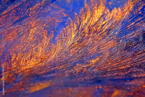 Icy frosty ornate pattern of thin ice on the window in the background of the dawn.