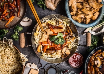 Asian kitchen table with food bowls, wok , stir fry , chopsticks and ingredients on background, top view