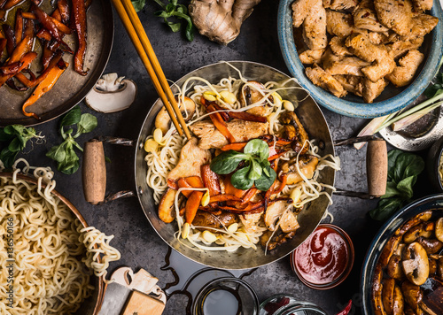 Asian kitchen table with food bowls, wok , stir fry , chopsticks and ingredients on background, top view