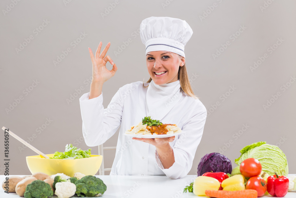 Cheerful female chef is showing ok sign while holding prepared meal. Cheerful female chef is showing ok sign while holding prepared meal.