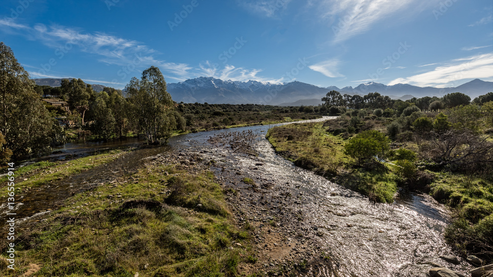 Shallow stream in Corsica with snow capped mountains in distance