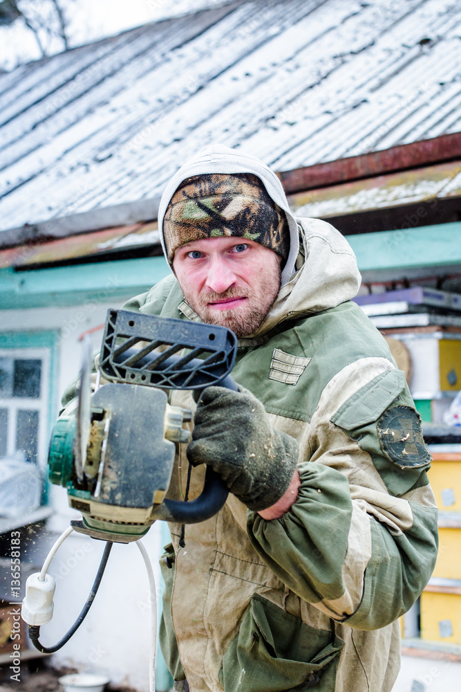 Obraz premium Man angry in military clothes. Work picked up a power saw. Man scares chainsaw an opponent in the street in winter