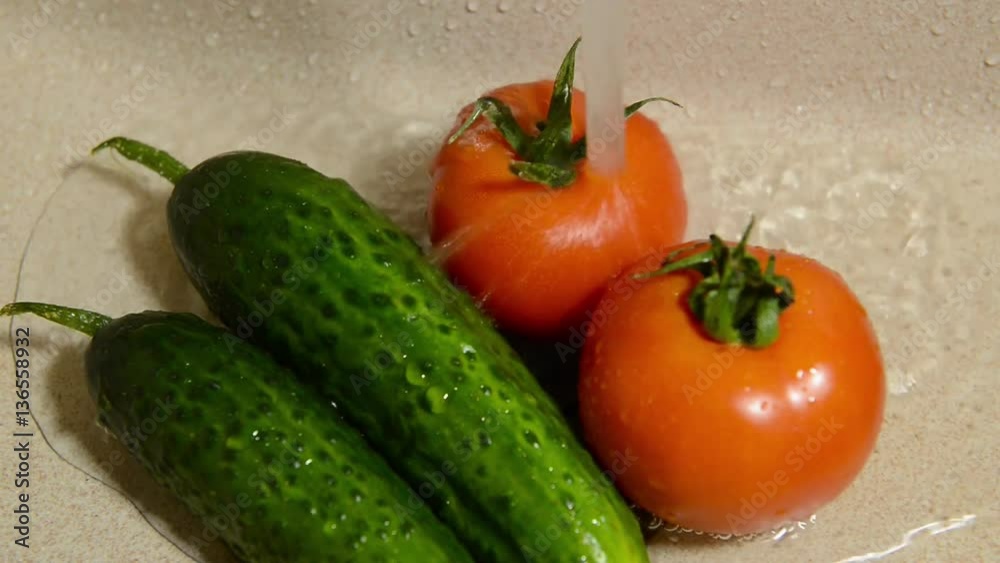Wash vegetables in a ceramic sink. Fresh tomatoes and cucumbers under running water Wash vegetables in a ceramic sink. Fresh tomatoes and cucumbers under running water