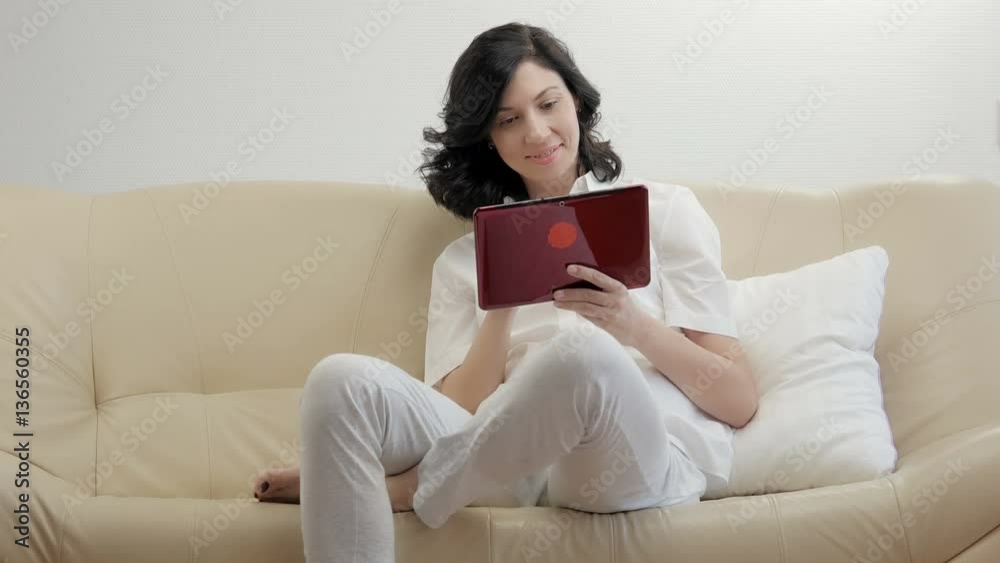 Woman sitting in sofa and websurfing on digital tablet.
Woman sitting in sofa and websurfing on digital tablet.