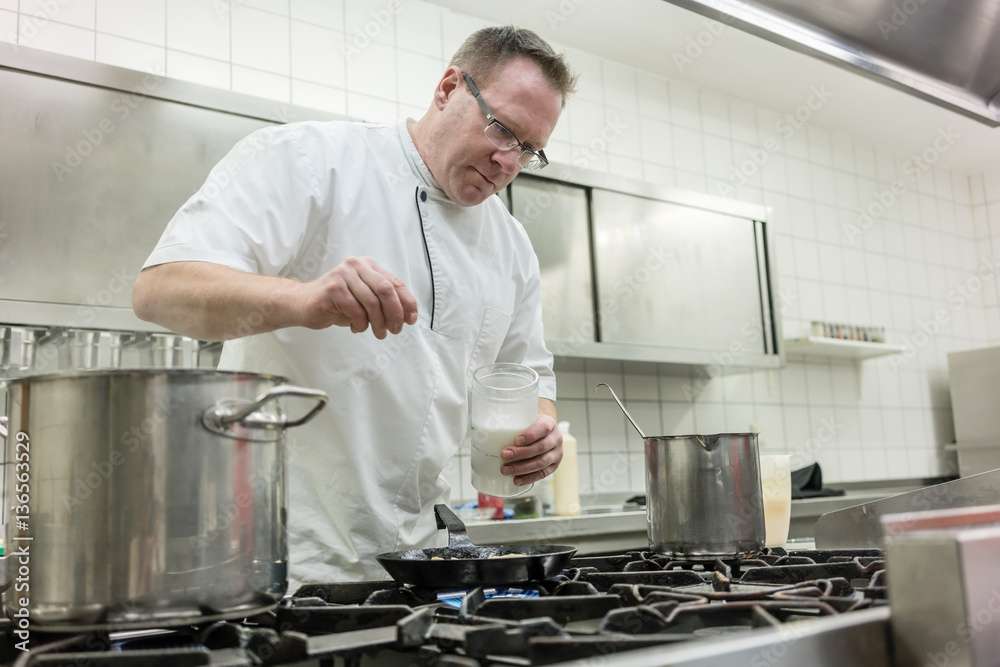 Koch bereitet Pfannkuchen in Küche zu und gießt den Teig in die Pfanne Koch bereitet Pfannkuchen in Küche zu und gießt den Teig in die Pfanne