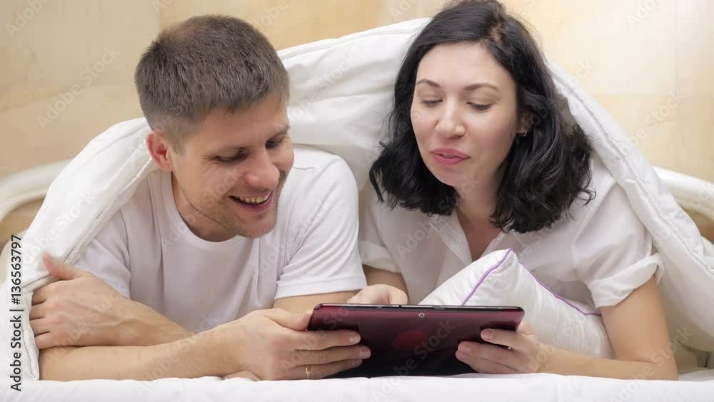 Couple using their tablet together and chatting in bed at home. Couple using their tablet together and chatting in bed at home.