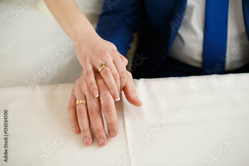 hands of the bride and groom with rings on a white table
