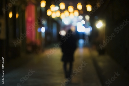 A lonely man is walking in a shiny street. Which is illuminated with chinese lanterns. 