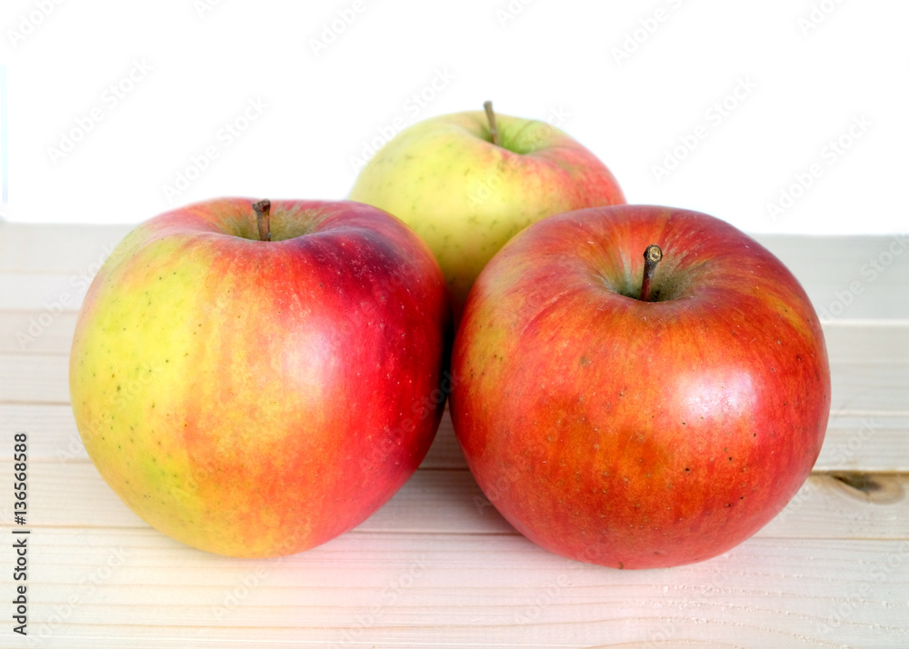 Three big ripe red apples in beige wooden shelf on white background front view closeup Three big ripe red apples in beige wooden shelf on white background front view closeup