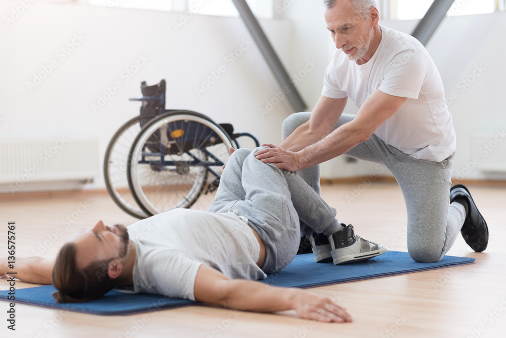 Proficient general practitioner stretching the disabled in the gym Proficient general practitioner stretching the disabled in the gym