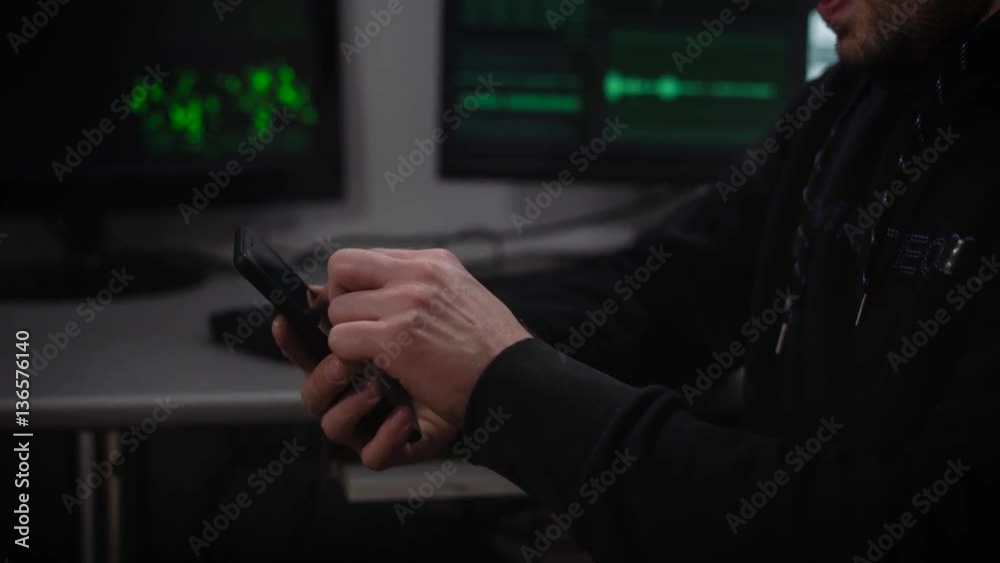 Serious man with brown hair, glasses on the eyes, stubble beard, wearing a black hoodie intently typing on your phone which is located in a dark room, like a secret bunker Serious man with brown hair, glasses on the eyes, stubble beard, wearing a black hoodie intently typing on your phone which is located in a dark room, like a secret bunker