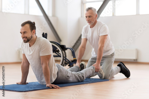 Cheerful physical therapist stretching the handicapped in the gym