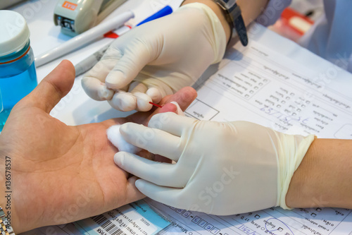 A nurse takes blood from a finger on the analysis photo