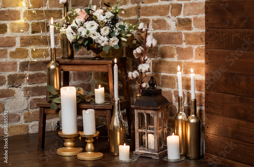 Many burning candles on candlesticks and lantern with fresh flower arrangement
