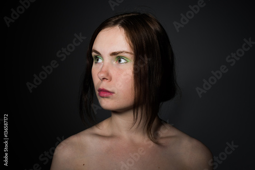 Portrait of a beautiful brunette girl with green make and white skin on a dark background 