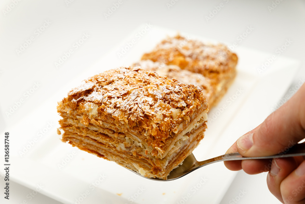 French Napoleon Cake of puff pastry with sour cream on a white plate close-up. Nutritious dessert. Selected Focus French Napoleon Cake of puff pastry with sour cream on a white plate close-up. Nutritious dessert. Selected Focus