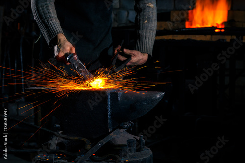 The blacksmith manually forging the molten metal on the anvil in smithy with spark fireworks photo