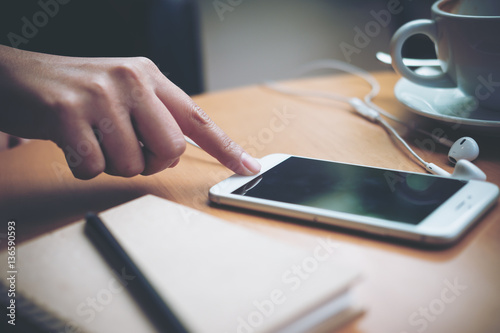 A woman's hand touching and using a smart phone on wooden table in modern cafe  