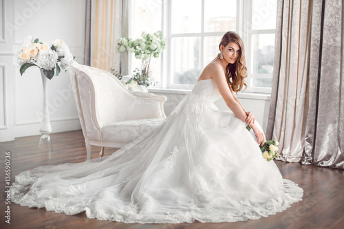 Fotografie Bride in beautiful dress sitting resting on sofa indoors