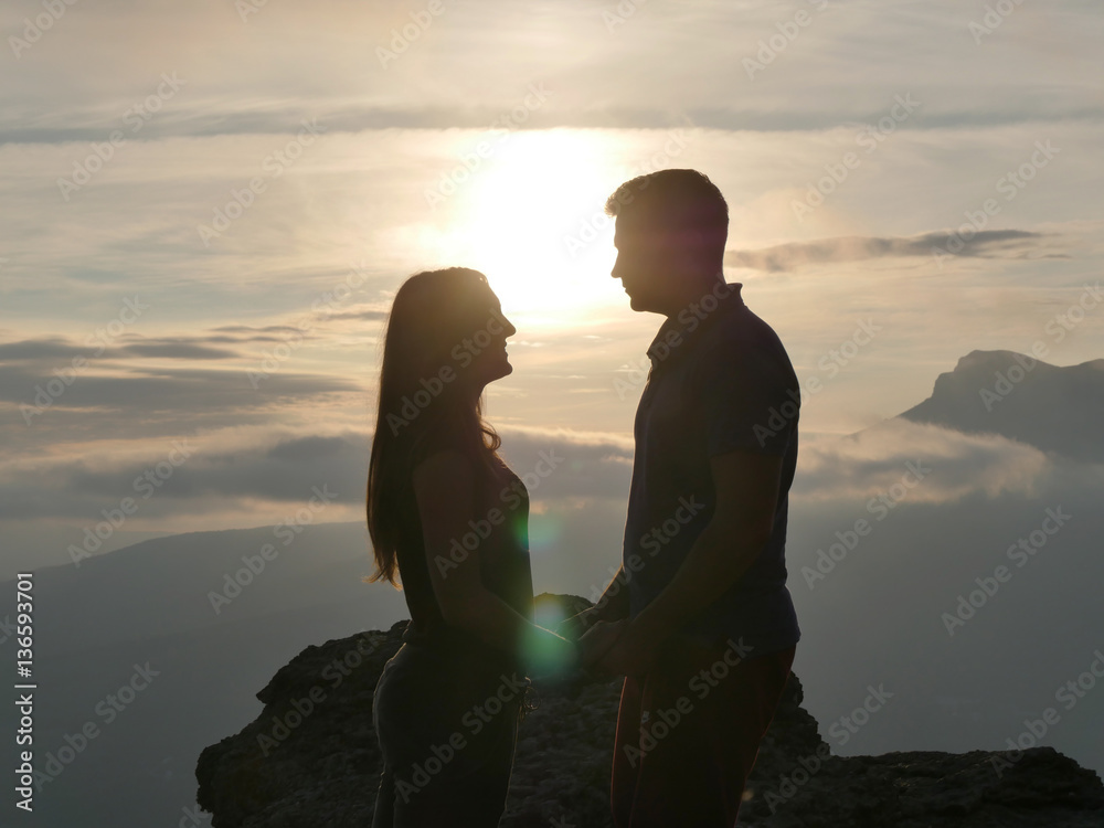 Silhouettes of young couple standing on a mountain and looking t