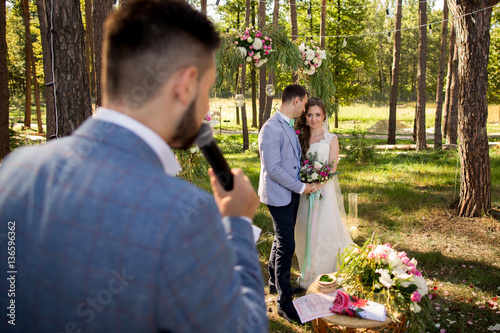Leading or master of ceremonies, bride and groom at wedding ceremony with decorations and arch in rustic style