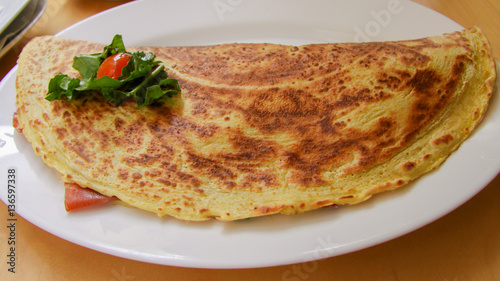 Pancake stuffed with tomato, cheese and green salad on white plate.  © Irina