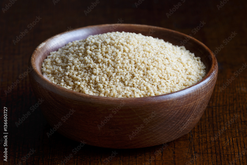 Dry couscous in brown wooden bowl isolated on dark wood. Dry couscous in brown wooden bowl isolated on dark wood.
