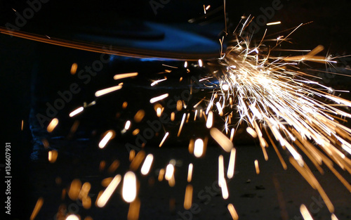 Worker grinding a metal construction with grinding wheel, lots of sparks in factory