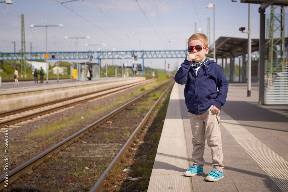 Adorable kid boy waiting for a train at the railway station in a sunny day. Child ready for traveling by train. Train station. Dreaming of traveling. Sunny day at the railway station Adorable kid boy waiting for a train at the railway station in a sunny day. Child ready for traveling by train. Train station. Dreaming of traveling. Sunny day at the railway station